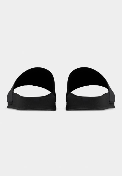 Ζευγάρι μαύρα σανδάλια τύπου σλάιντ με καμπυλωτούς ιμάντες, εμφανιζόμενα από μπροστά πάνω σε απλό φωτεινό φόντο.