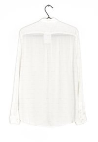 Camicia bianca a maniche lunghe esposta su una gruccia, caratterizzata da un delicato motivo tessuto, polsini con bottone e orlo arrotondato.