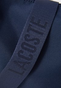 Marineblå strukturert stoff med en matchende stropp som har subtilt broderte tekster på en veske.