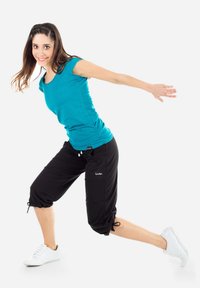 Camicetta turchese a maniche corte abbinata a pantaloni neri cropped. Il modello indossa sneaker bianche; i pantaloni presentano orli regolabili e tasche laterali.
