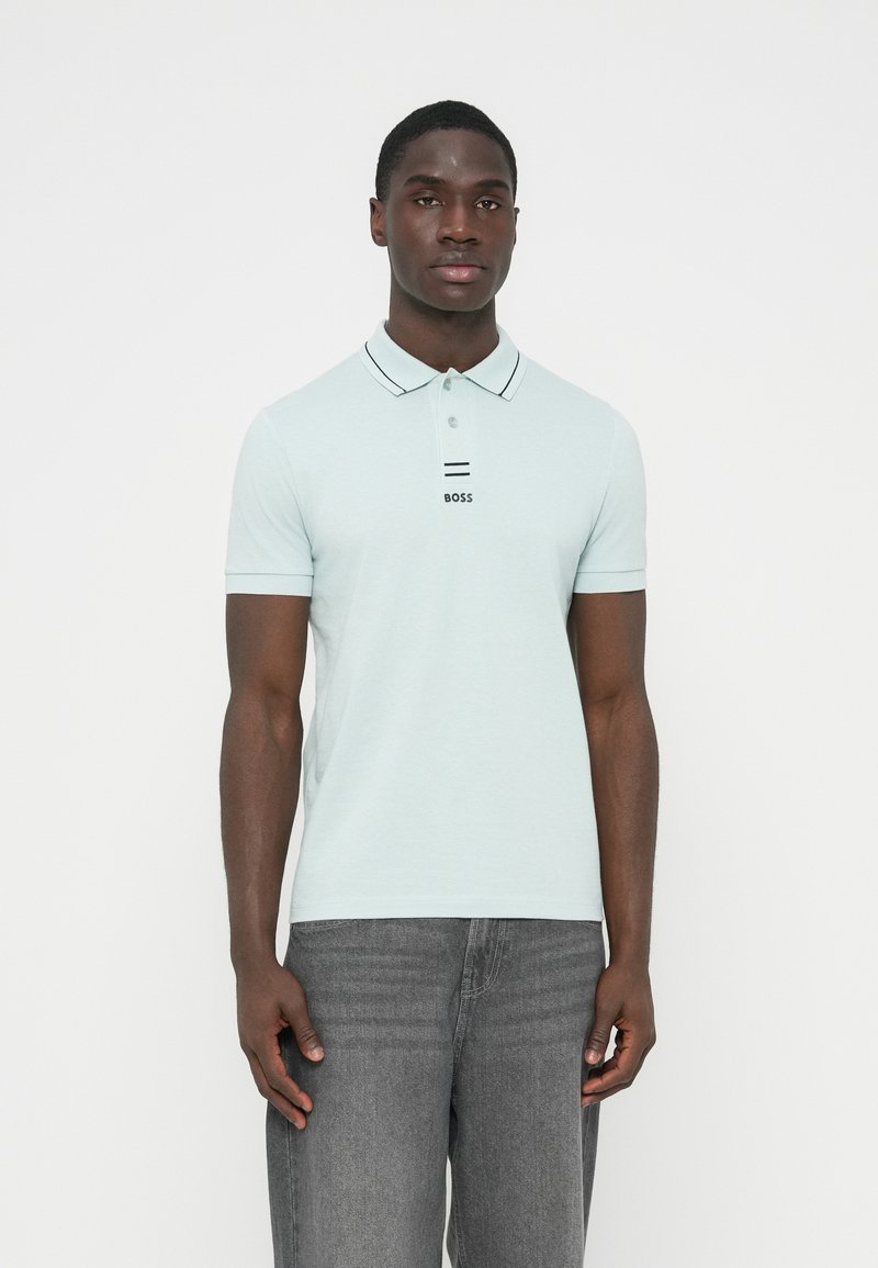 Ανοιχτό μπλε πόλο μπλουζάκι με γιακά με μαύρες ρίγες και λογότυπο "BOSS" μπροστά. Φορεμένο με γκρι τζιν, διαθέτει κοντά μανίκια και εφαρμοστή γραμμή.