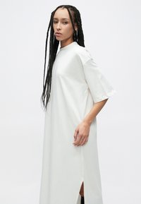 Hvit knelang bomulls kjole med korte ermer, sidesliss, rund hals og avslappet passform. Jevn tekstur og minimalistisk design.