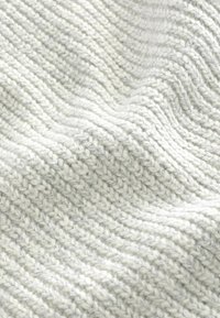 Tissu tricoté en gris clair avec des côtes texturées variées, présentant des fils épais et douillets créant une apparence douce et mélangée.