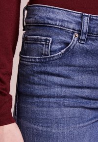 Denimjeans med en bleknad blå färg, med en framficka, fransade kanter och standardknäppning med knapp och dragkedja.