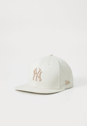 Casquette de baseball blanche avec logo New York Yankees beige brodé sur le devant et petit logo de marque beige sur le côté.