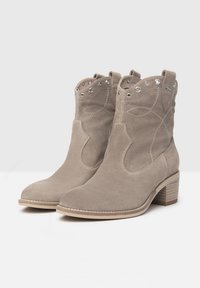 Bottines en daim gris avec des découpes décoratives, des accents métalliques et un talon empilé. Présentent des détails de couture et une forme classique.