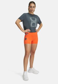 Grijze t-shirt met wit grafisch logo, gecombineerd met feloranje shorts met zijkanten en een zwart patch. Witte sneakers.