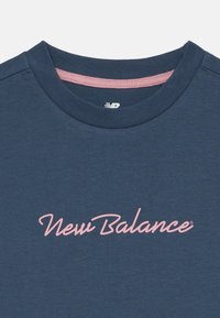 T-shirt azul de gola redonda com o logótipo em script rosa "New Balance" centrado no peito e um acabamento rosa na gola interior.