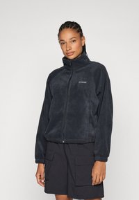 Giacca in pile nera con colletto alto e chiusura con zip, con logo sul lato sinistro del petto e polsini e orlo a costine.