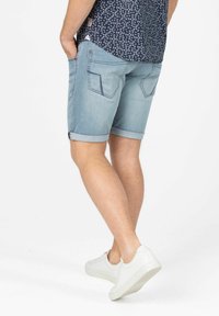 Light blue denim shorts with rolled cuffs, back pockets featuring stitched accents, worn with white sneakers and patterned shirt.