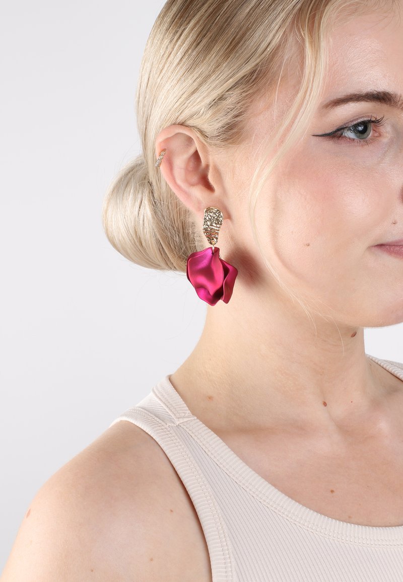 Orecchini in tonalità oro con una parte superiore testurizzata e un design a goccia scultorea in satin rosa. Gli orecchini sono grandi e attirano l'attenzione.