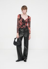 Top transparent negru cu un model floral roșu, asortat cu pantaloni negri din piele ecologică cu talie înaltă și o geantă mică neagră.