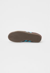 Brun lädersneakersula med ett texturerat honungsbegrepp. Har turkosa och svarta ränder längs sidan för kontrast.