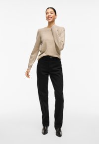 Suéter beige de manga larga combinado con pantalones de pana negros de cintura alta. La modelo lleva botas de tobillo. Tejido suave y diseño ajustado.
