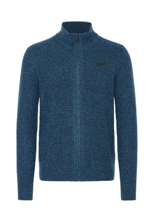 Blå zip-up tröja med en strukturerad stickad design, hög krage och en liten svart etikett som accentuerar vänster sida.