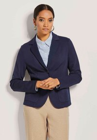 Marineblazer aus weichem Stoff, mit einem einzigen Knopf, Spitzrevers, schlanker Schnitt, kombiniert mit einem hellblau gestreiften Hemd. Minimalistisches Design, lässige Eleganz.