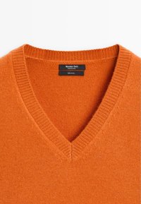 Pull en laine orange avec col en V et étiquette noire indiquant Massimo Dutti, fabriqué en Chine, 100 % laine.