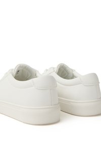 Zapatillas blancas con un acabado mate suave, perfil bajo, punta redonda y suela de goma texturizada. Se ven los cordones y el interior suave.