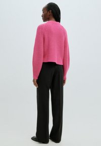 Pull en laine rose à design court, texture côtelée et manches longues, accompagné d'un pantalon large noir.