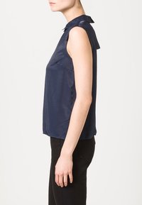 Marinblå ärmlös blus med krage och slät textur. Har en avslappnad passform och en sidoklyfta för enkel rörelse.