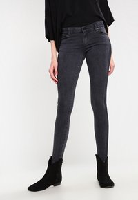 Černé úzké džíny z hladké elastické látky. Vysoký pas a elegantní střih, doplněné černými kotníkovými botami.