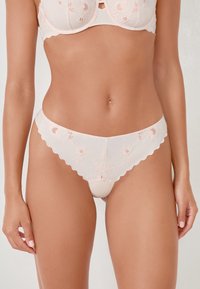 Ensemble de lingerie rose clair orné de dentelle, avec broderies florales sur le soutien-gorge et la culotte assortie ; tissu lisse, bords festonnés.