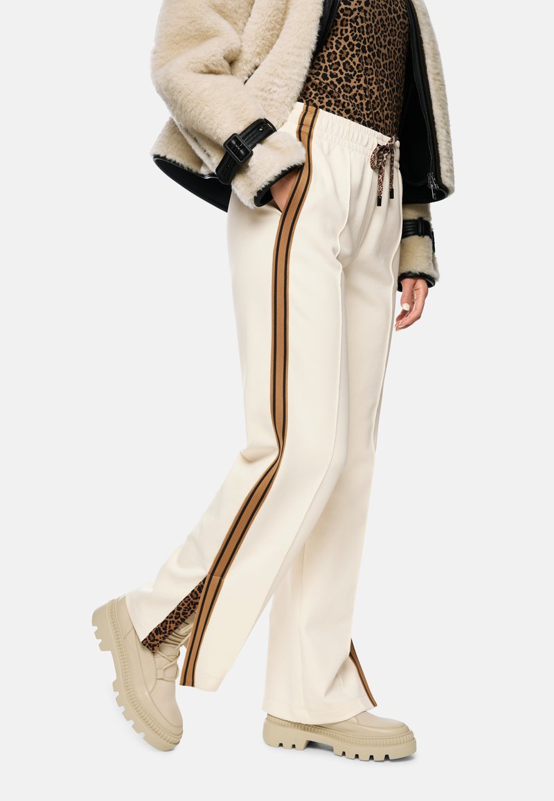 Cream-colored pants with side brown stripes, paired with beige platform shoes. The outfit features a textured jacket and a leopard print top.