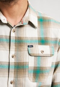 Bruin en blauwgroen geruite katoenen overhemd met knopen, voorzien van een borstzak, houten knopen, een kraag en subtiele rode accenten.