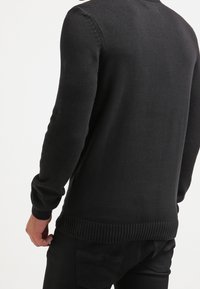 Maglione nero a maglia con maniche lunghe, polsini e orlo a coste, texture liscia, design semplice, senza motivi o decorazioni visibili.