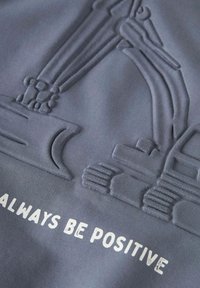 Pelēks kokvilnas audums ar iegravētu būvmašīnu dizainu un izcilu tekstu: "MAKSĀDIET VIENMĒR POZITĪVI" baltā krāsā.