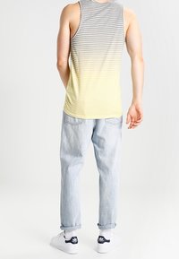 Top de tirantes a rayas con degradado de gris a amarillo, combinado con jeans de mezclilla azul claro y zapatillas blancas con acentos azul oscuro.