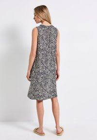 Sukienka bez rękawów w czarno-kremowy wzór z abstrakcyjnym motywem liści. Miękki materiał, długość do kolan, luźny krój i okrągły dekolt.