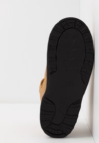 Bruna lädersneakers med en texturerad svart gummisula, präglad med distinkta mönster och en synlig logotyp på sula.