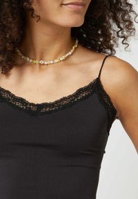 Zwarte camisole met kantdetail bij de halslijn, met dunne spaghettibandjes. Draagt een multikleurige kralenhalssnoer, waaronder smiley-gezicht en bloemaccenten.