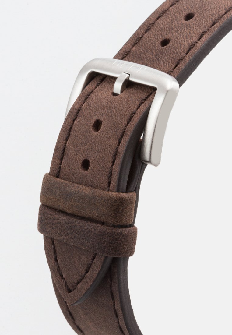 Correa de reloj de cuero marrón con hebilla de metal plateado y múltiples agujeros de ajuste sobre un fondo blanco.