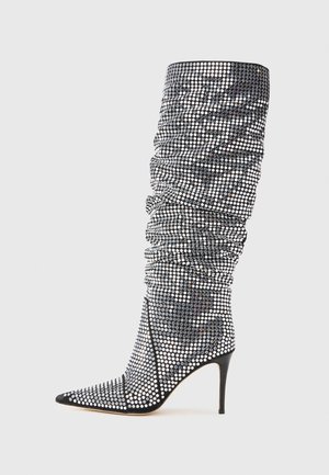 Čizme na visoku petu do koljena s crno-bijelim ukrasima od dragog kamenja, oštrim vrhom i nabranom teksturom koja naglašava štiklu.