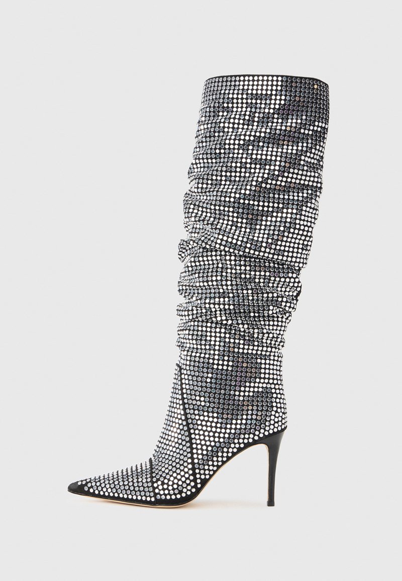 Cizmă cu toc înalt, până la genunchi, cu ornamente bijuterii alb-negru, vârf ascuțit și textură strânsă care accentuează tija.