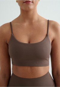 Bruine crop top met verstelbare spaghettibandjes. Gladde textuur en aangesloten ontwerp, met een rechte halslijn en geribbelde details aan de zoom.