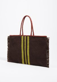 Geweven tote bag met bruine textuur, franjes aan de randen en drie verticale gele strepen. Voorzien van gevlochten rode handvatten.