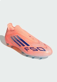 Botas de fútbol de color coral brillante con rayas azules de Adidas y el lettering "FSO", diseñadas para jugar en terrenos firmes con tacos moldeados.