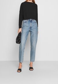 Black ribbed long-sleeve top, light blue high-waisted jeans, and black slide sandals. Accessories include a small black handbag.