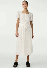 White midi dress with puff sleeves and a square neckline, featuring button closures and eyelet embroidery. Worn with black platform sandals.