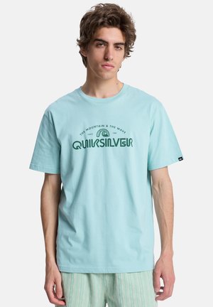 Hellblaues Baumwoll-T-Shirt mit einem aufgedruckten grünen Logo, Text und Wellengrafik. Kurze Ärmel, Rundhalsausschnitt und lockere Passform.