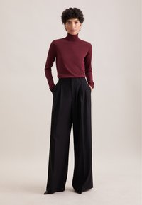 Maglione a collo alto bordeaux con maniche lunghe abbinato a pantaloni neri a gamba larga in vita alta. Tessuto liscio e design sartoriale.