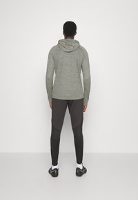 Tenue de sport composée d'un hoodie à manches longues vert et de leggings noirs avec un motif texturé. Détail de capuche et design ajusté.