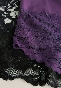 Kúsok čipky v čiernej a purpurovej farbe s jemne vykreslenými vlnitými okrajmi a kvetinovými vzormi, vrstvené spolu pre kontrastnú textúru a farbu.