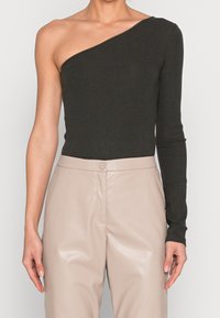 Schwarzer gerippter One-Shoulder Bodysuit mit langem Ärmel, kombiniert mit hochgeschnittenen beigefarbenen Kunstlederhosen mit einer vorderen Verschluss.