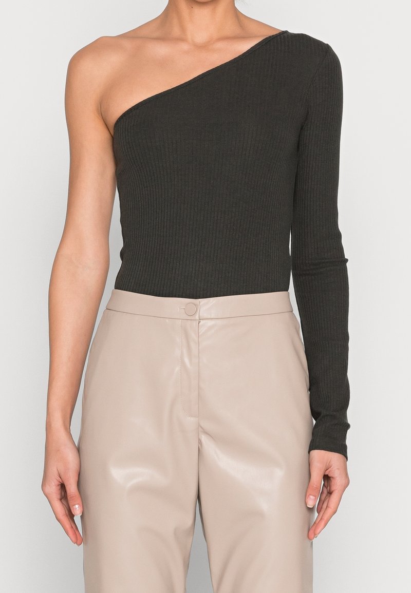 Schwarzer gerippter One-Shoulder Bodysuit mit langem Ärmel, kombiniert mit hochgeschnittenen beigefarbenen Kunstlederhosen mit einer vorderen Verschluss.