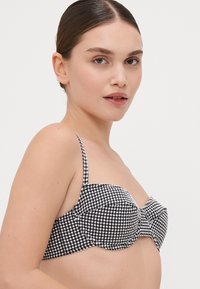 Črno-bela gingham bikinka zgornji del z oporo z žico, nastavljivimi naramnicami in oblazinjenimi skodelicami; tkanina prikazuje karo vzorec.