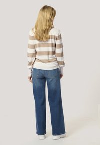 Sweter w paski w beżowym i białym kolorze, z okrągłym dekoltem i ściągaczami, w połączeniu z luźnymi niebieskimi dżinsami i białymi trampkami.